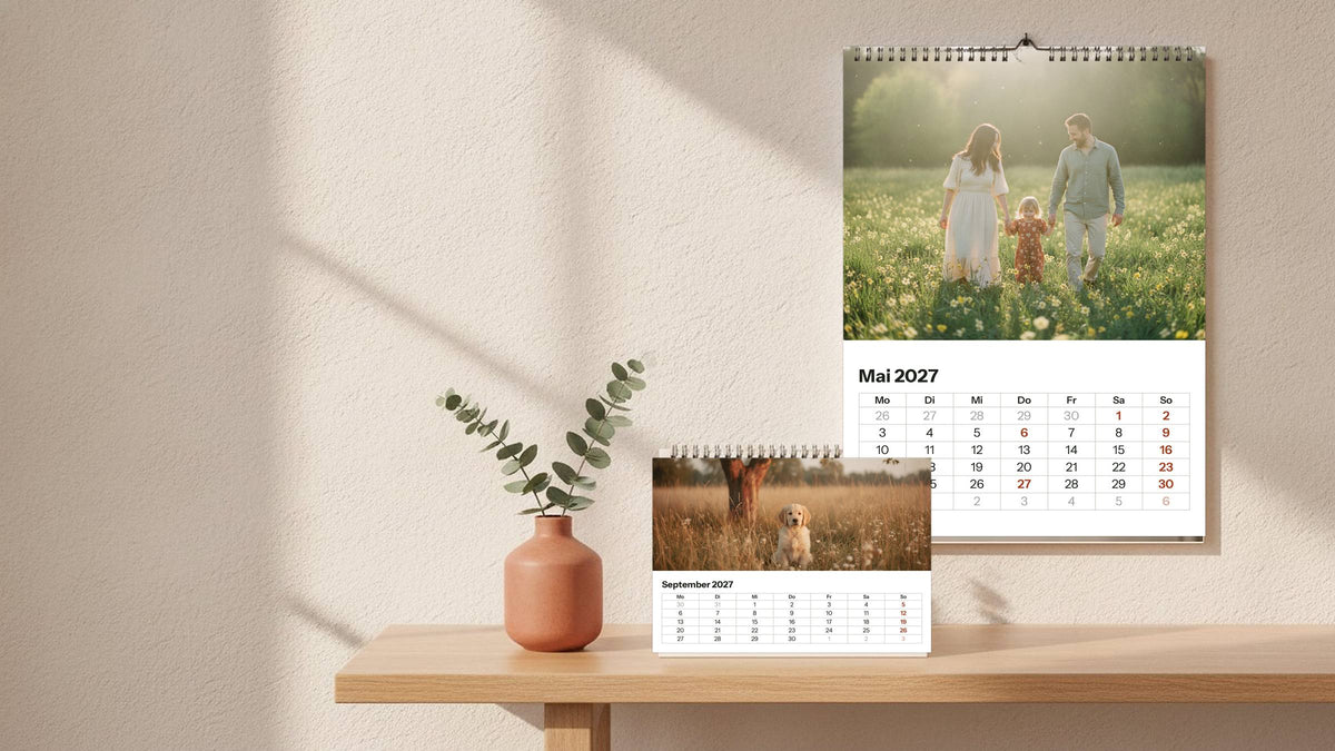 Dein Fotokalender im Wohnraum: Wandkalender A4 mit Familienfoto und Monatsraster Mai 2027, davor ein Tischkalender mit Welpenfoto und September-Raster, Eukalyptus in Terrakotta-Vase