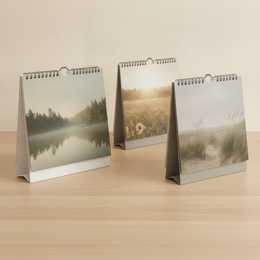 Drei Tischkalender mit unterschiedlichen Stützkonstruktionen nebeneinander auf einer Holzfläche